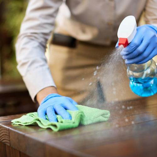 Close-up of waitress disinfecting tables at outdoor cafe.